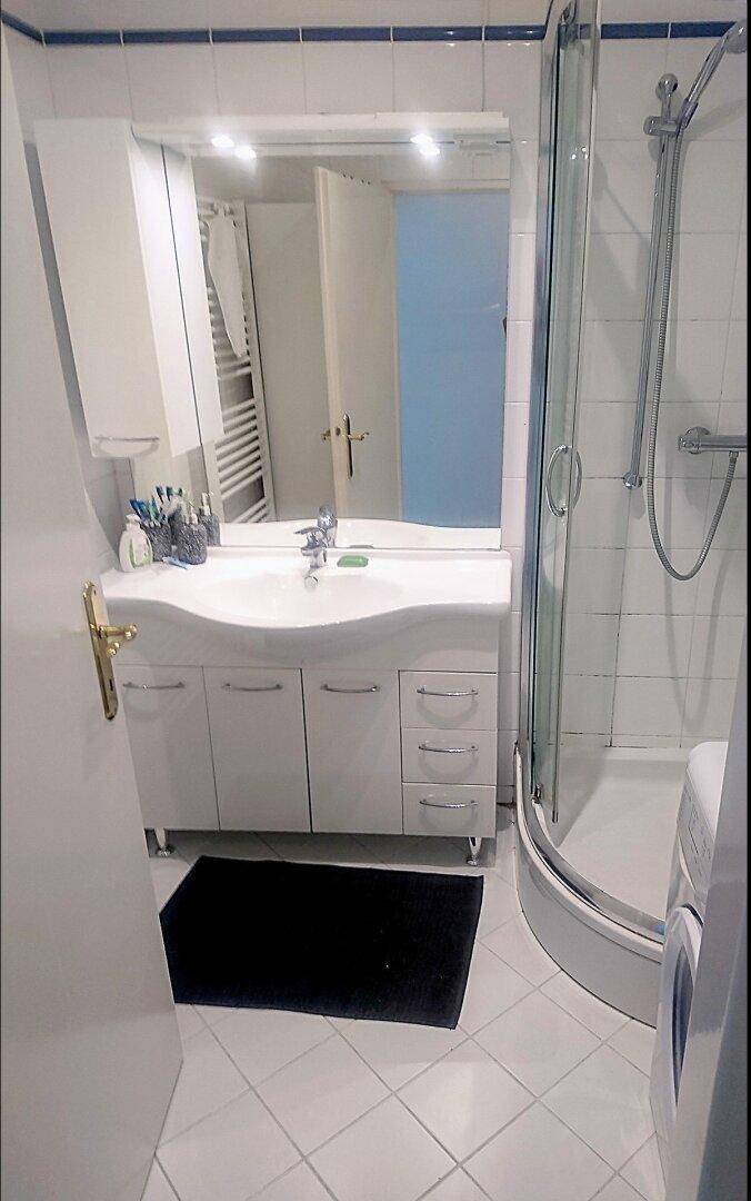 Badezimmer mit Duschkabine, Waschbecken mit Unterschrank und weiß-blauen Fliesen.