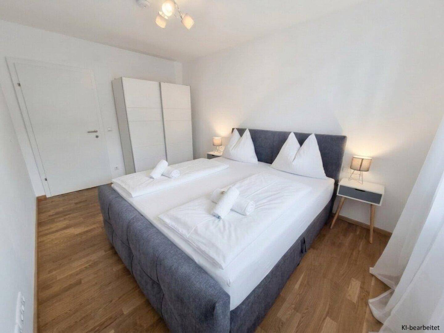 Helles Schlafzimmer mit Doppelbett, Nachttischen, Kleiderschrank und Holzboden.