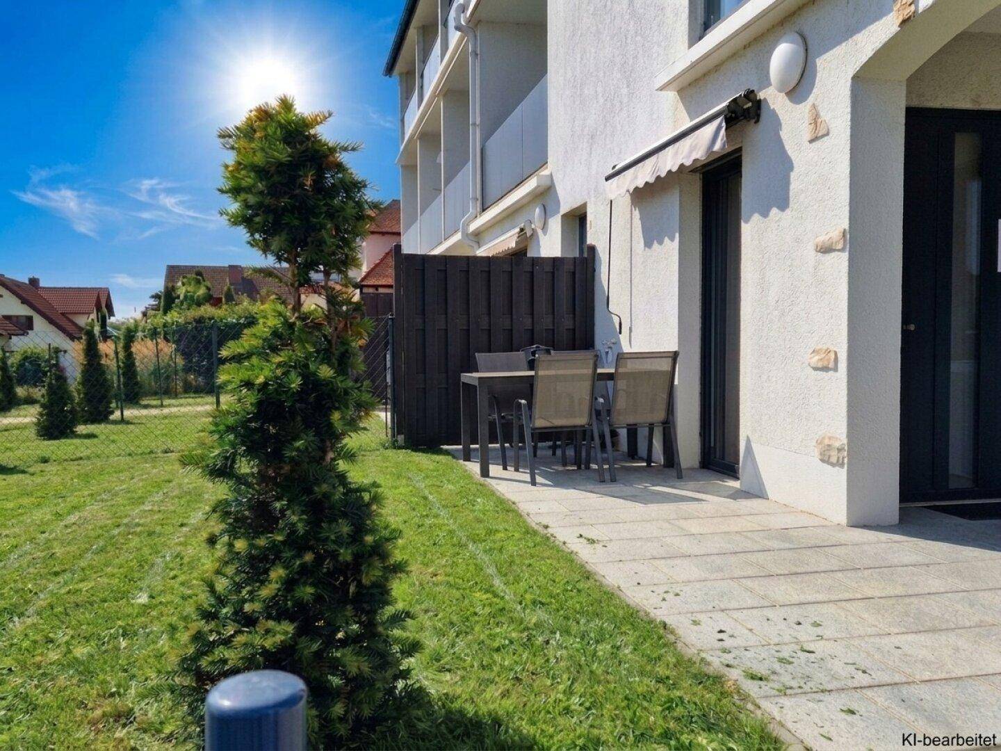 Sonniger Terrassenbereich mit Sitzgelegenheiten und angrenzendem Rasen vor der modernen Fassade.