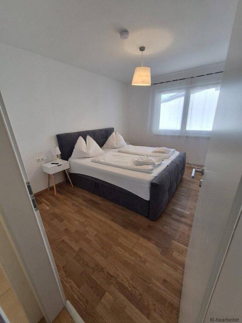 Schlichtes Schlafzimmer mit Doppelbett, Holzboden und Fenster für natürliches Licht.
