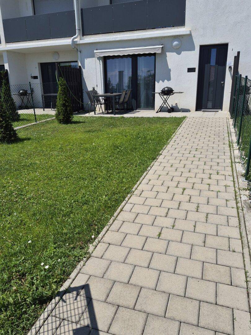 Gepflegter Gartenbereich mit Terrasse, Gartenmöbeln und Grill vor einem modernen Neubau.