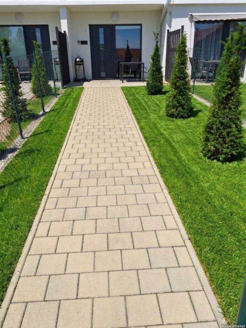 Gepflasterter Weg führt zu modernen Wohneinheiten mit gepflegtem Rasen und kleinen Bäumen.