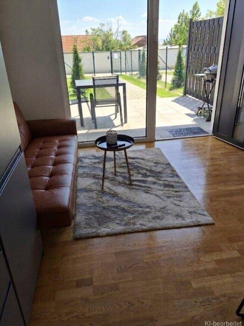 Gemütlicher Wohnbereich mit braunem Sofa, Holzboden und Zugang zu einer möblierten Terrasse.