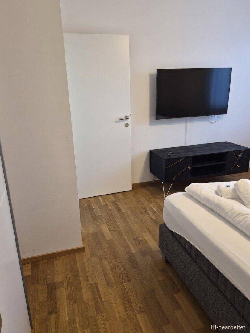 Schlafzimmer mit Holzboden, einem bequemen Bett und einem wandmontierten Fernseher.