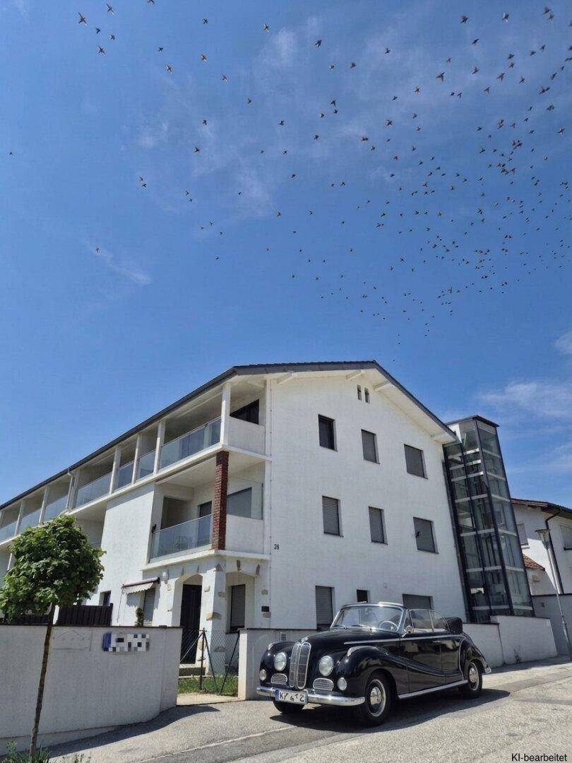 Modernes Gebäude mit weißer Fassade, Balkonen und einem externen Glasaufzug unter blauem Himmel.