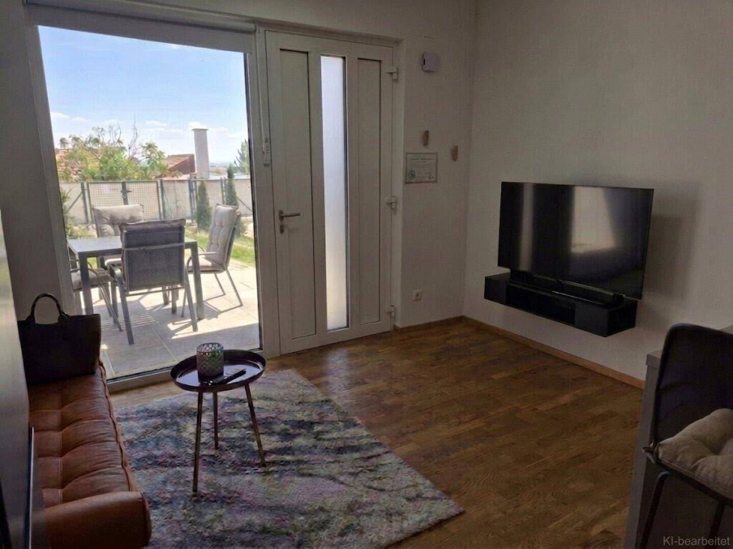 Heller Wohnbereich mit braunem Sofa, Holzboden und direktem Zugang zur möblierten Außenterrasse.