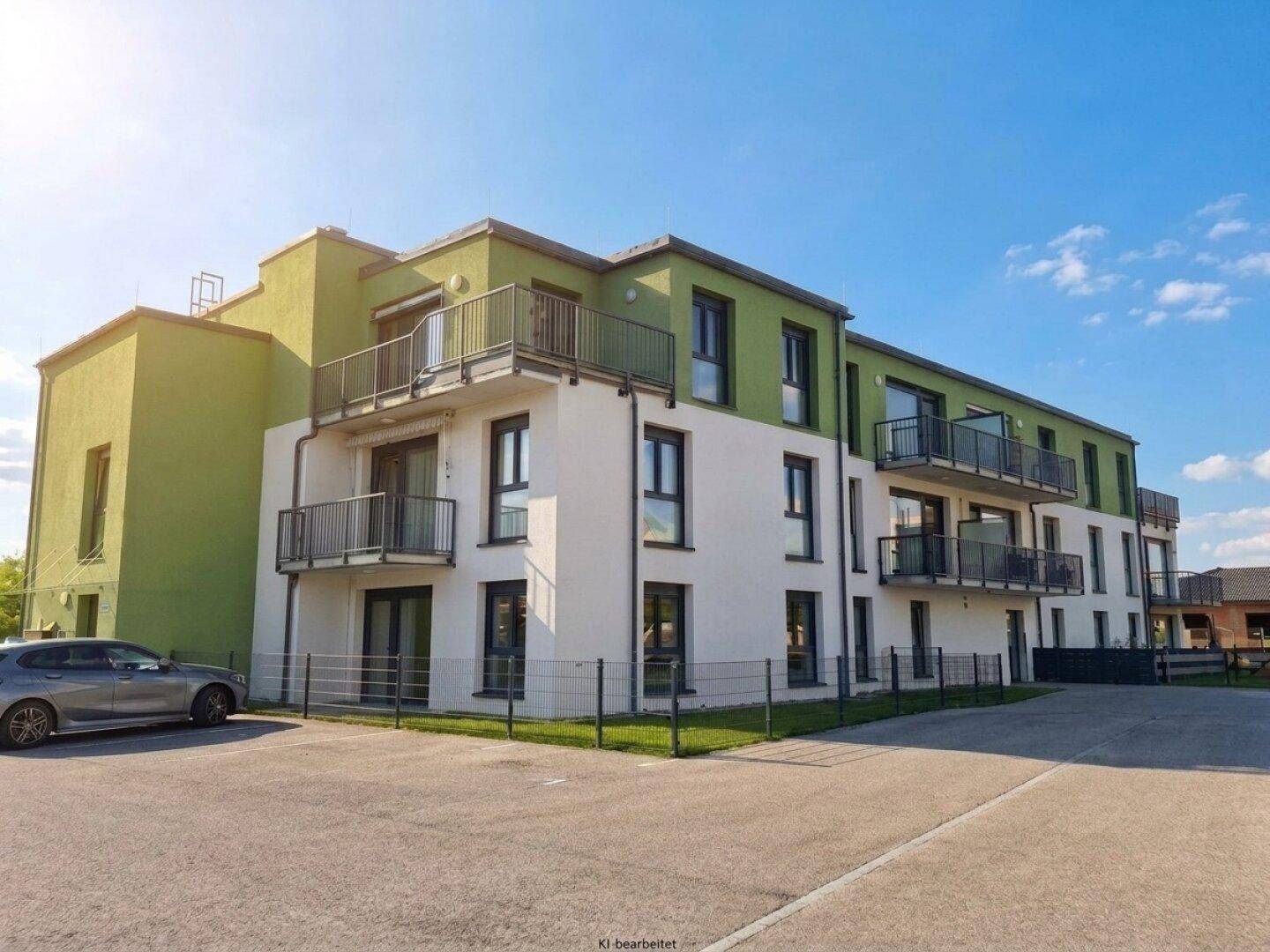 Neubau-Wohngebäude mit markanter grün-weißer Fassade, mehreren Balkonen und sonnigen Außenstellplätzen.