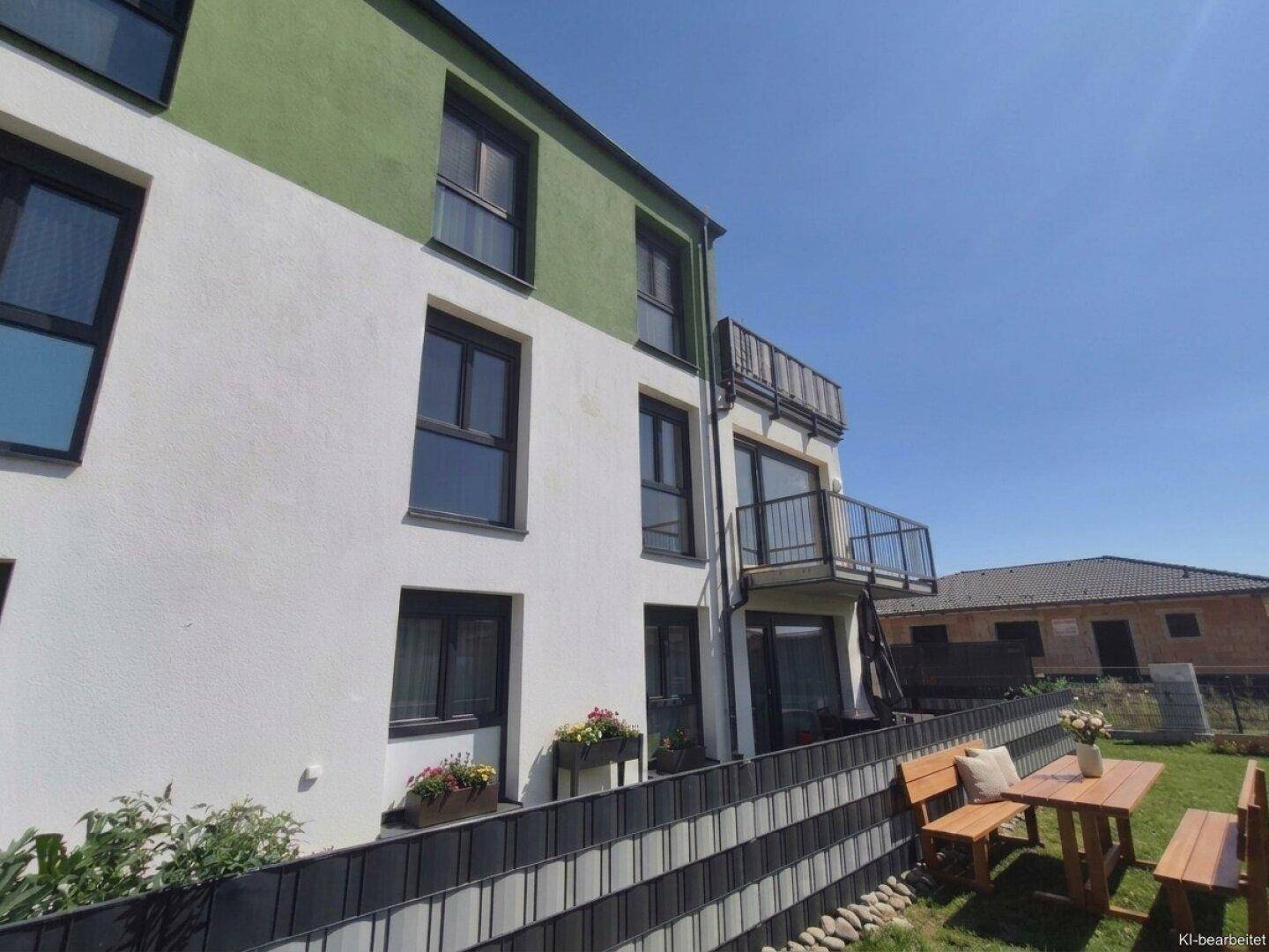 Moderne Wohnanlage mit weiß-grüner Fassade und einem kleinen Gartenbereich mit Sitzgelegenheiten.