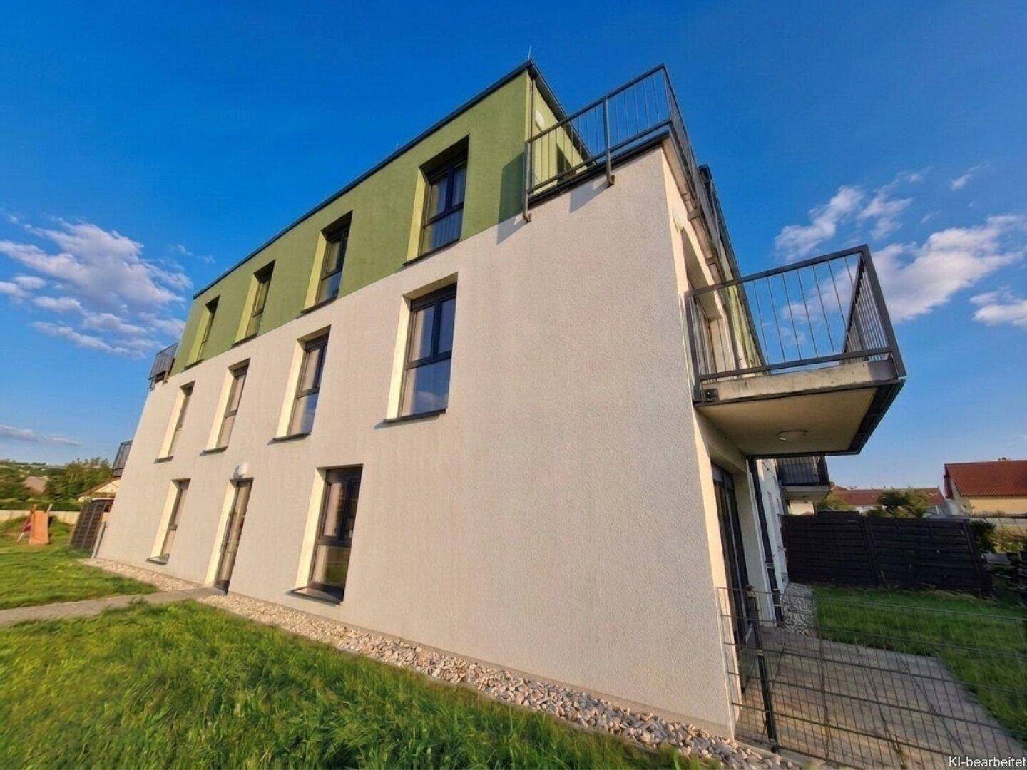 Seitenansicht eines modernen Neubaus mit weißer und grüner Fassade sowie Balkonen und Rasenfläche.