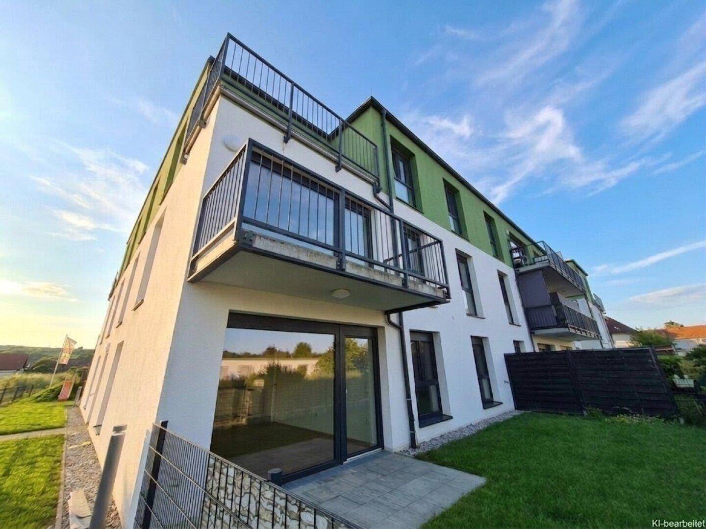 Modernes Mehrfamilienhaus mit weißer Fassade, grünen Akzenten und Balkonen unter blauem Himmel.