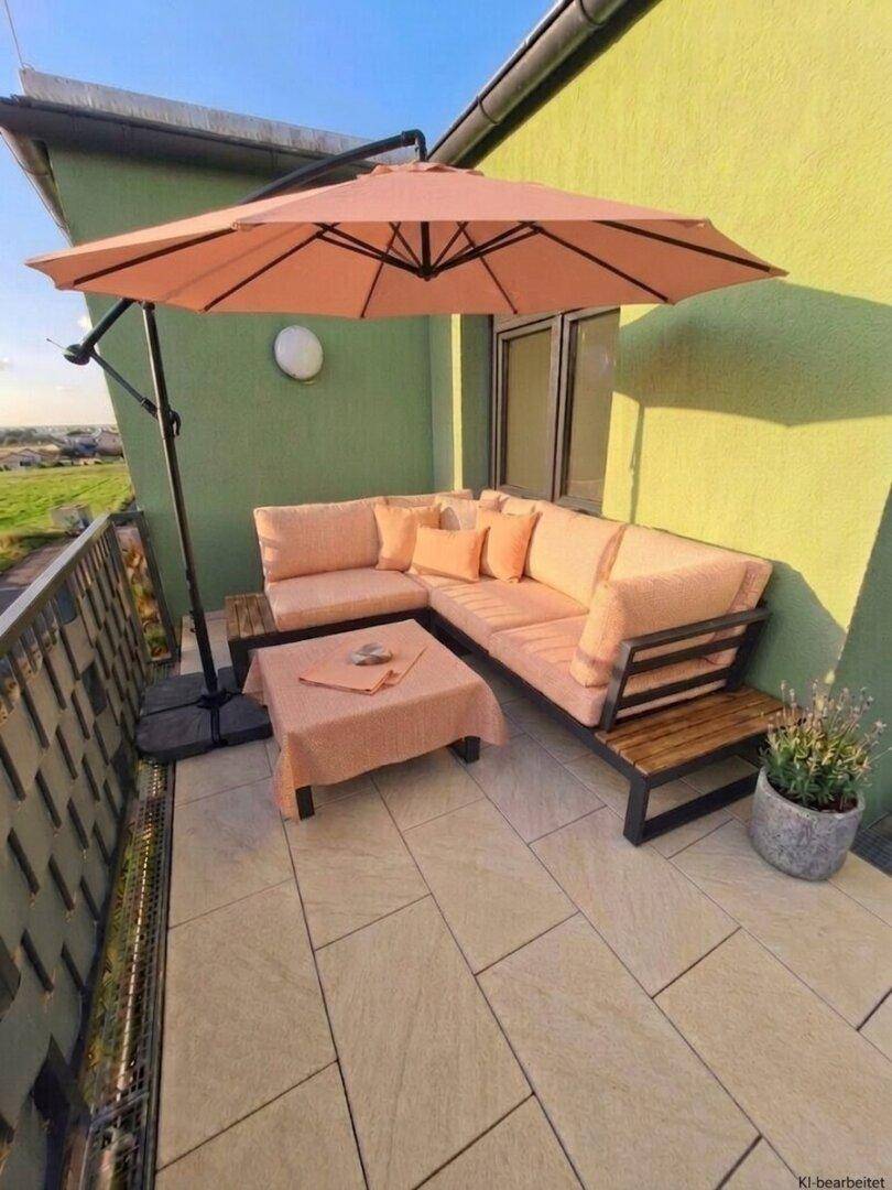 Gemütlicher Balkon mit beiger Lounge-Sitzgruppe, Sonnenschirm und weitem Blick ins Grüne.