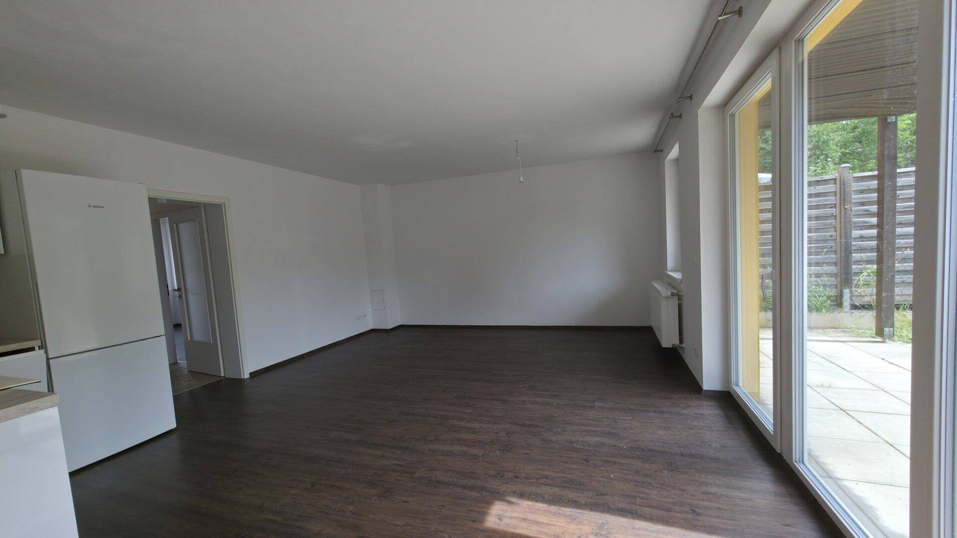 Geräumiger, heller Wohnbereich mit großen Fenstern und Zugang zur Terrasse.