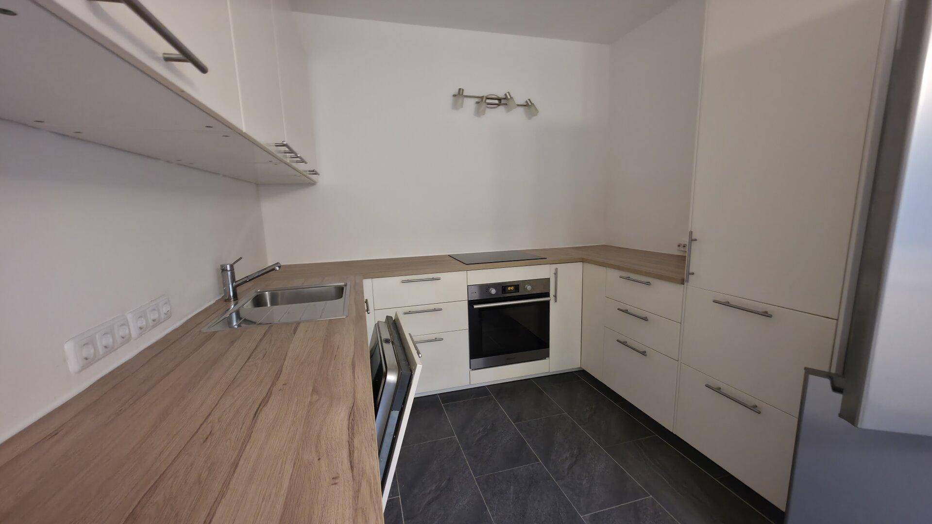 Moderne Einbauküche mit weißen Schränken, Holzarbeitsplatten und dunklem Fliesenboden.