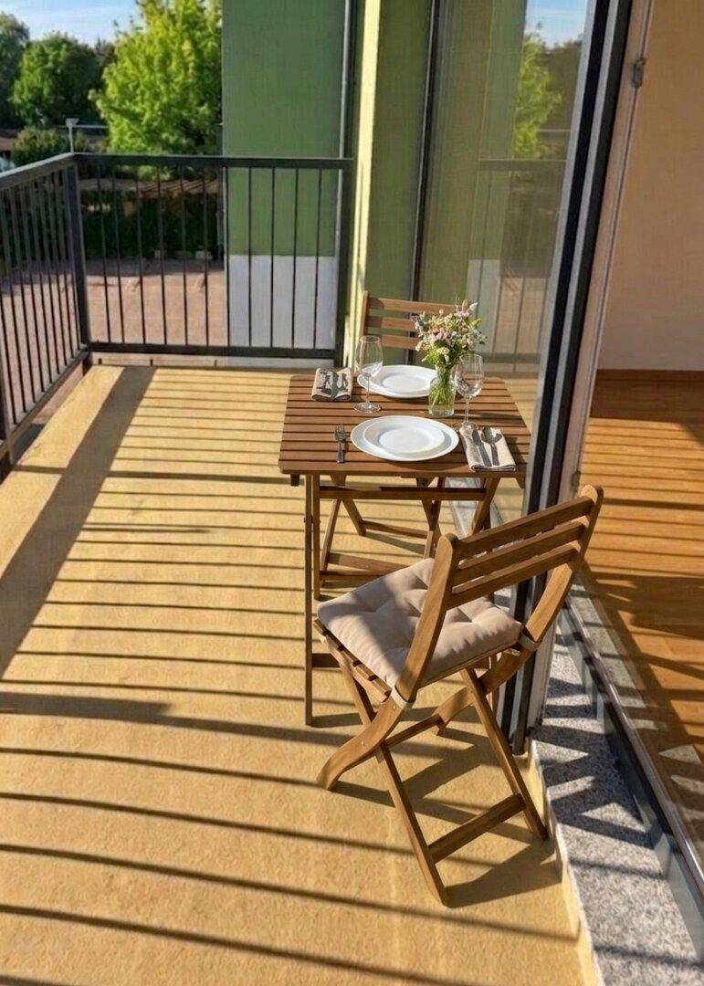 Heller Balkon mit Holztisch und Stühlen, ideal für Mahlzeiten im Freien mit Blick ins Grüne.