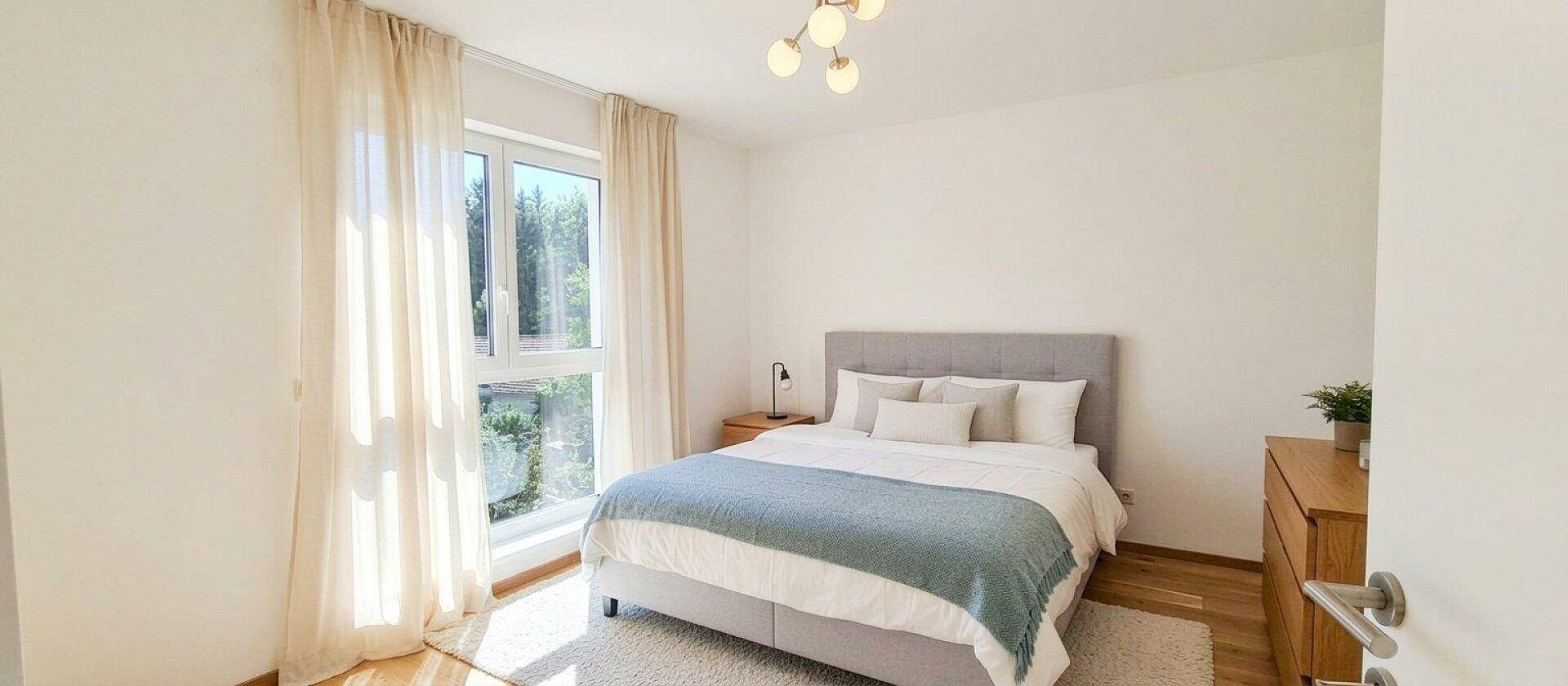Lichtdurchflutetes Schlafzimmer mit großem Fenster, Doppelbett und hellem Holzboden.