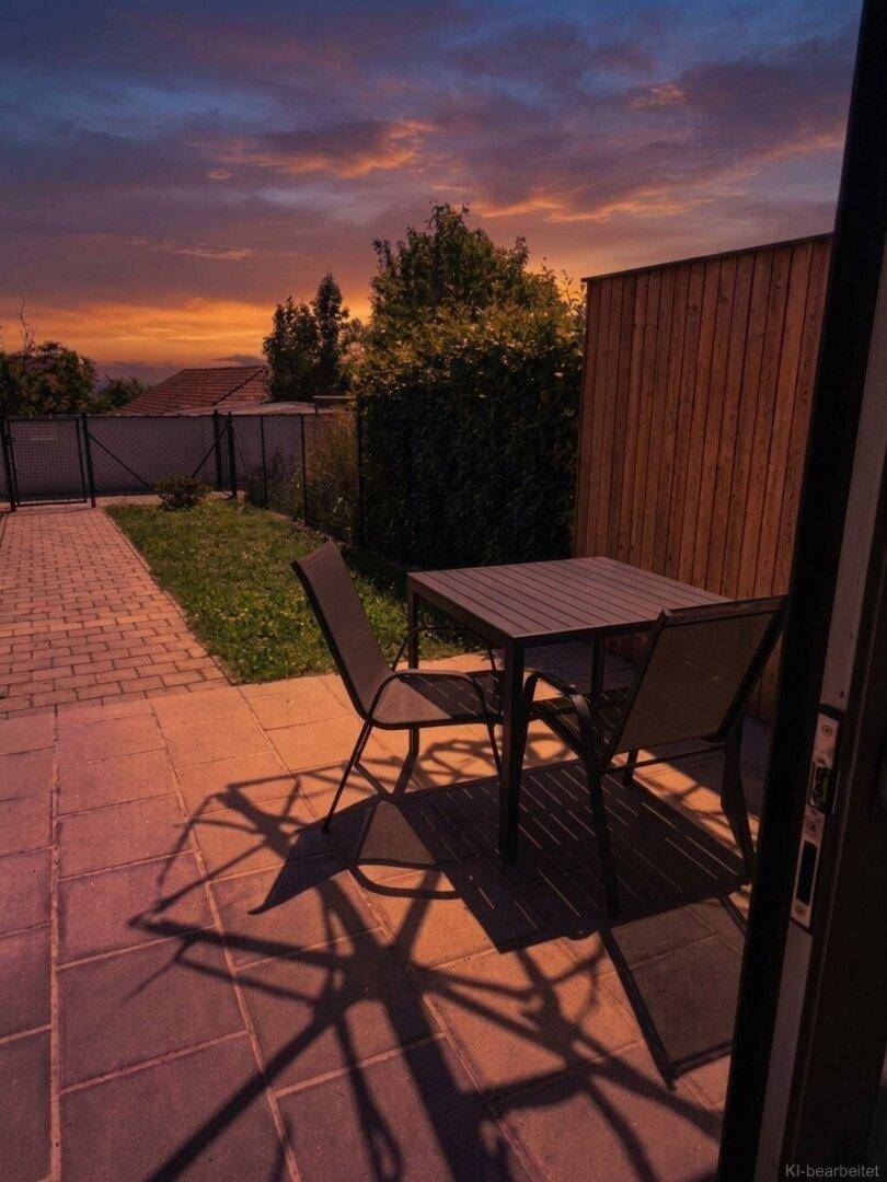 Gemütliche Terrasse mit Esstisch und Stühlen, umgeben von einer Holzverkleidung unter einem farbenfrohen Abendhimmel.