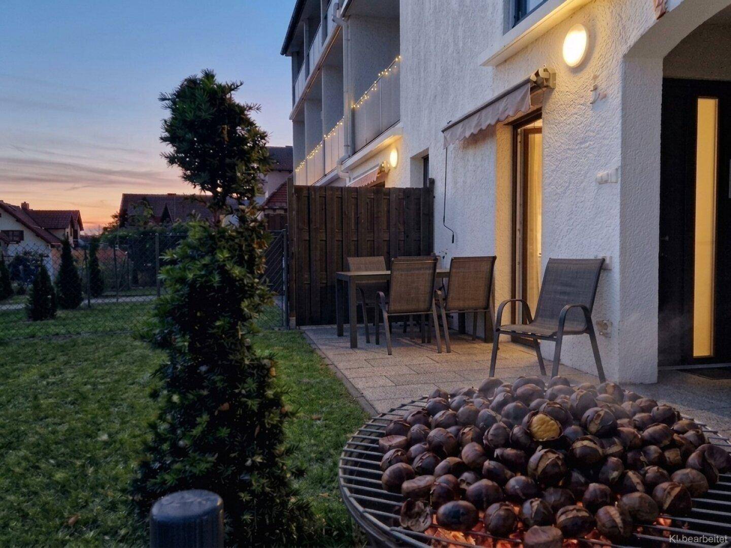Gemütliche Terrasse mit Grillplatz und Sitzgelegenheiten im Abendlicht, umgeben von Grünflächen.