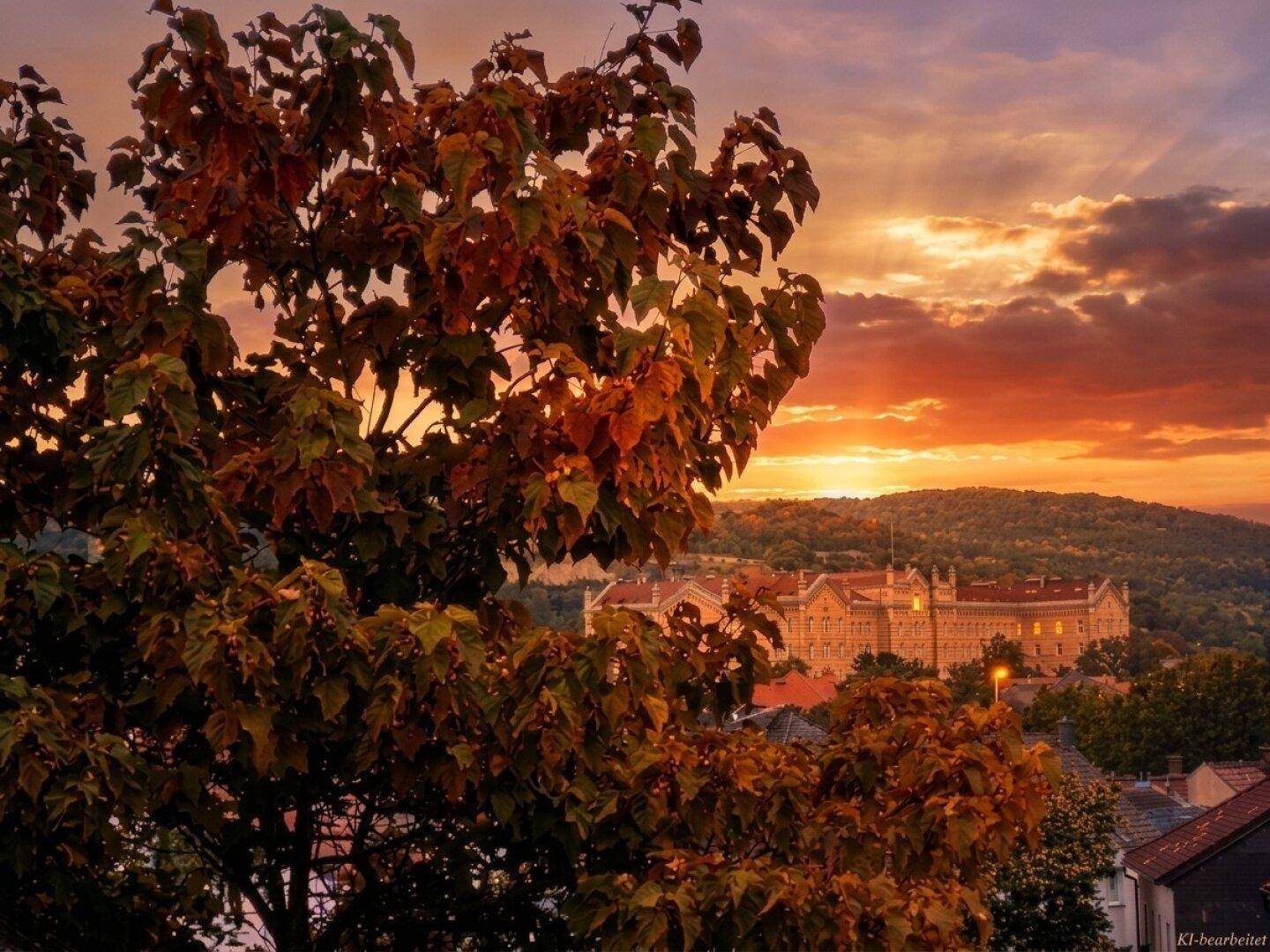 Malerischer Sonnenuntergang über einer hügeligen Landschaft mit historischen Gebäuden und Herbstbäumen.