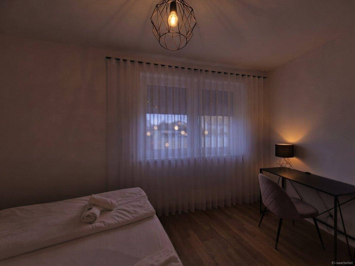 Schlafzimmer mit Holzboden, großem Fenster und einem Schreibtischbereich.