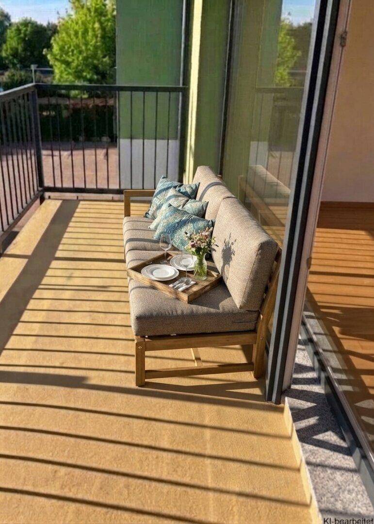 Sonniger Balkon mit bequemer Outdoor-Sitzgelegenheit und Blick ins Grüne, ideal für entspannte Stunden.