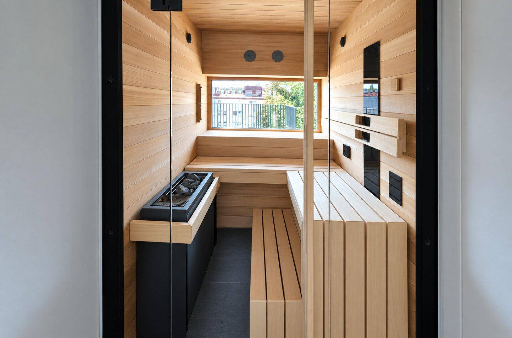 Moderne Sauna mit hellem Holz, integriertem Ofen und einem Fenster mit Ausblick.