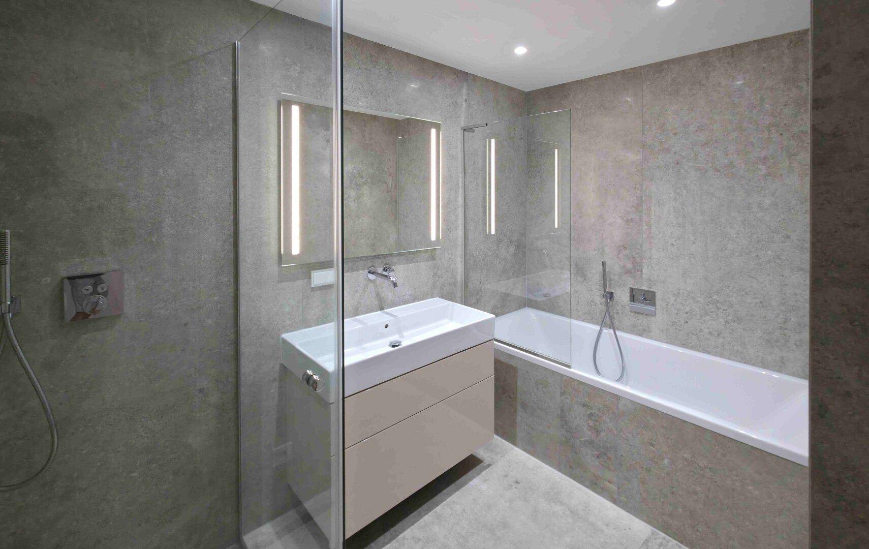 Modernes Badezimmer mit grauen Fliesen, Waschtisch und integrierter Badewanne mit Duschbereich.