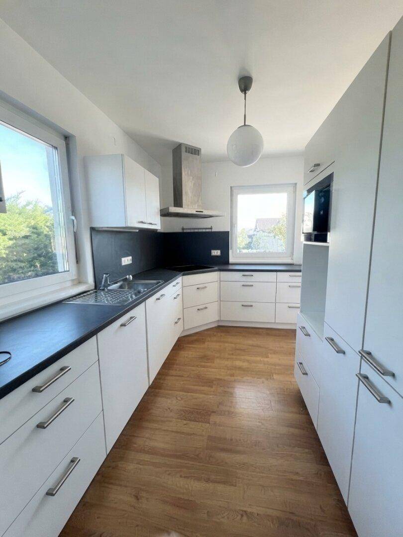 Moderne weiße Küche mit dunkler Arbeitsplatte, Holzboden und Fenster mit Ausblick.