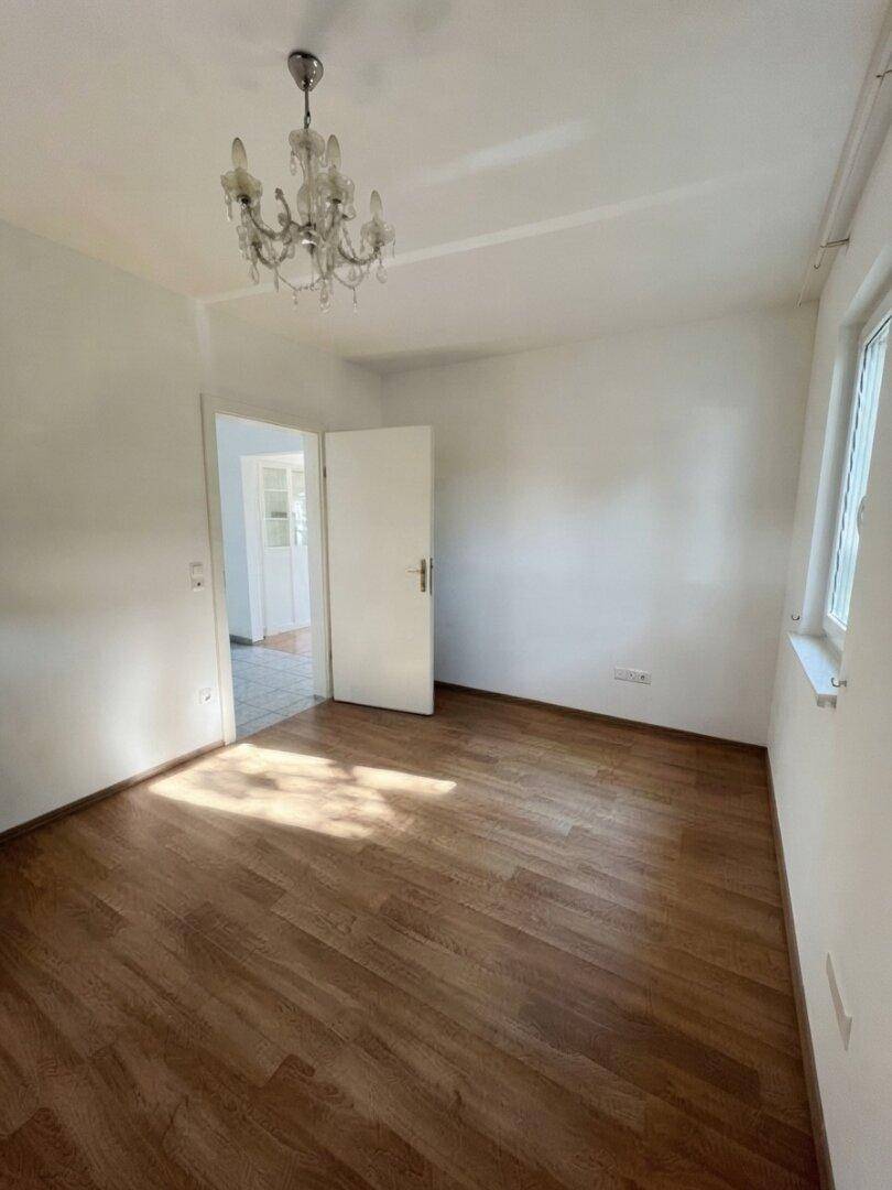 Helles Zimmer mit Holzboden, Kronleuchter und weiß gestrichenen Wänden.