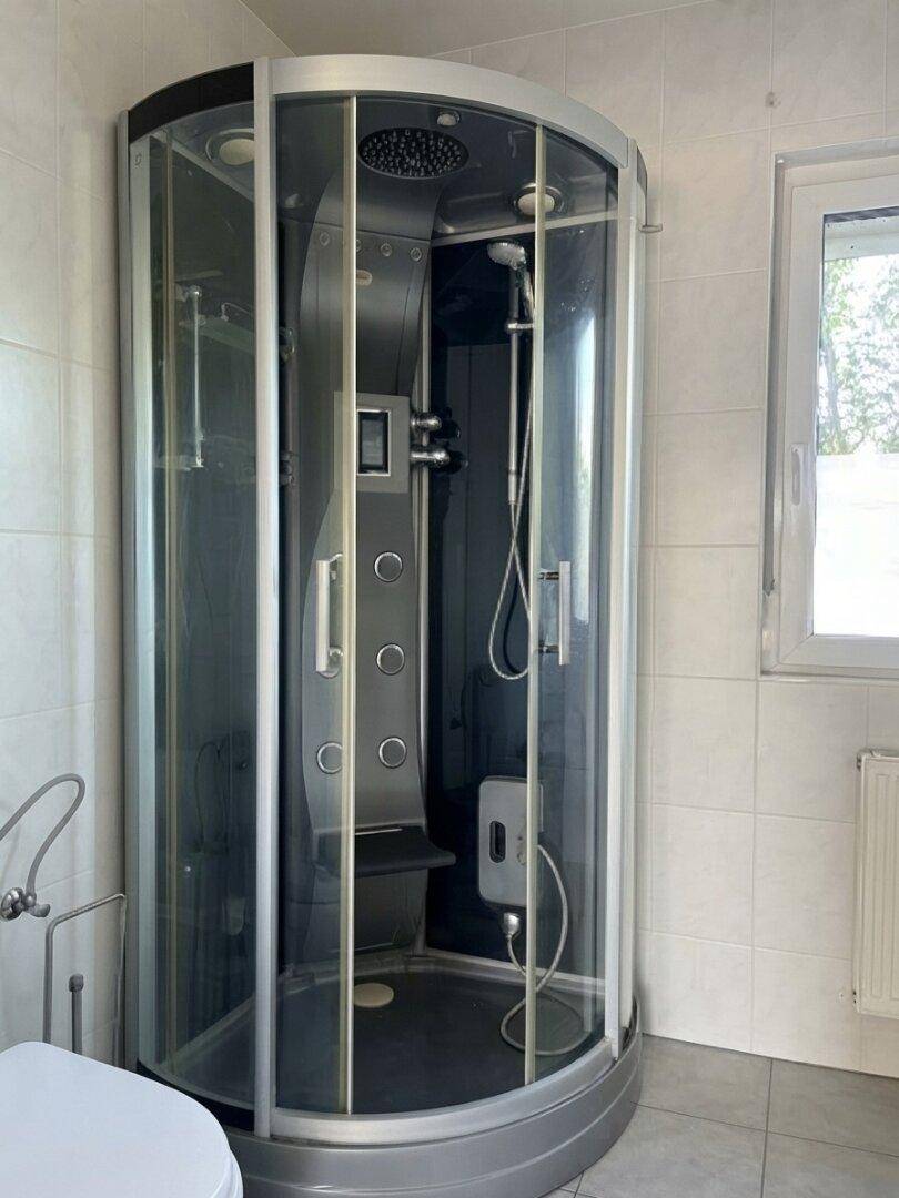 Badezimmer mit moderner Duschkabine, Fliesenboden und Fenster für Tageslicht.