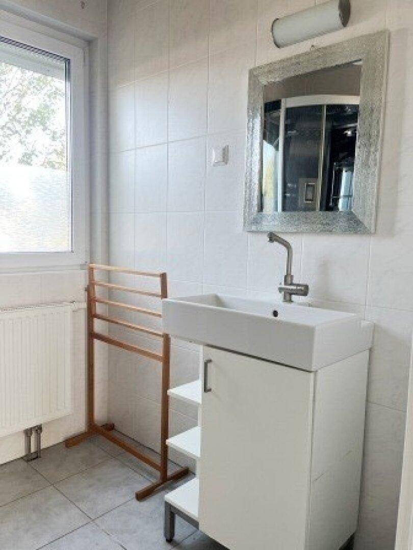 Badezimmer mit Waschbecken, Spiegel und Fenster, das viel Tageslicht hereinlässt.