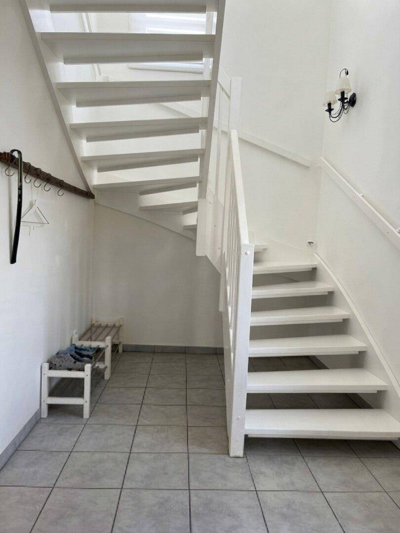 Heller Treppenaufgang mit weißen Stufen und Fliesenboden, der zum Obergeschoss führt.