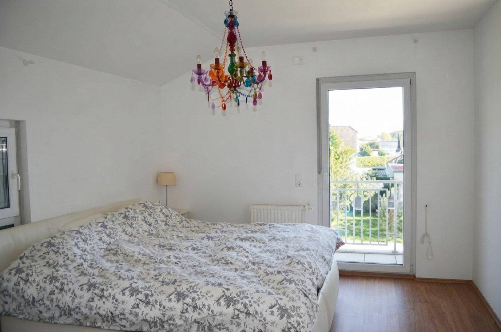 Schlafzimmer mit Doppelbett, Holzboden und farbenfrohem Kronleuchter, mit Balkonzugang.