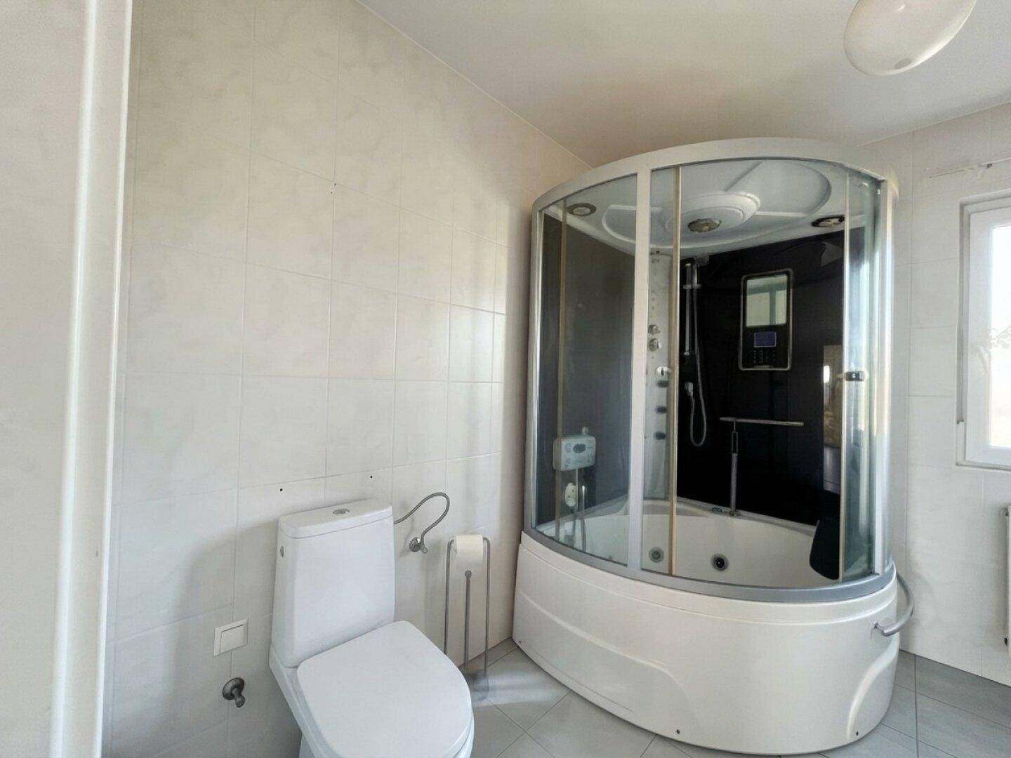 Badezimmer mit Toilette und großer Dusch-Whirlpool-Kabine, gefliesten Wänden und Boden.