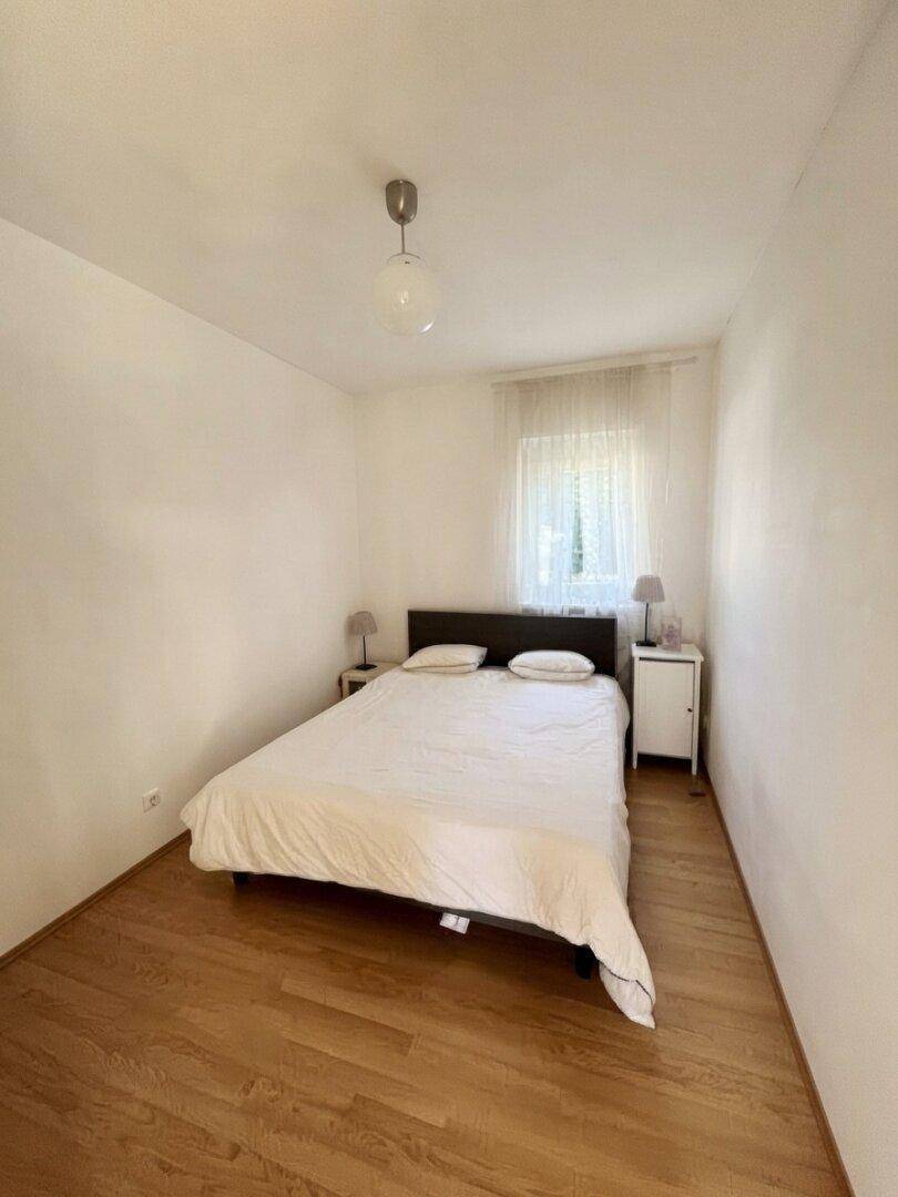 Gemütliches Schlafzimmer mit Holzboden, Fenster und einfacher, heller Einrichtung.