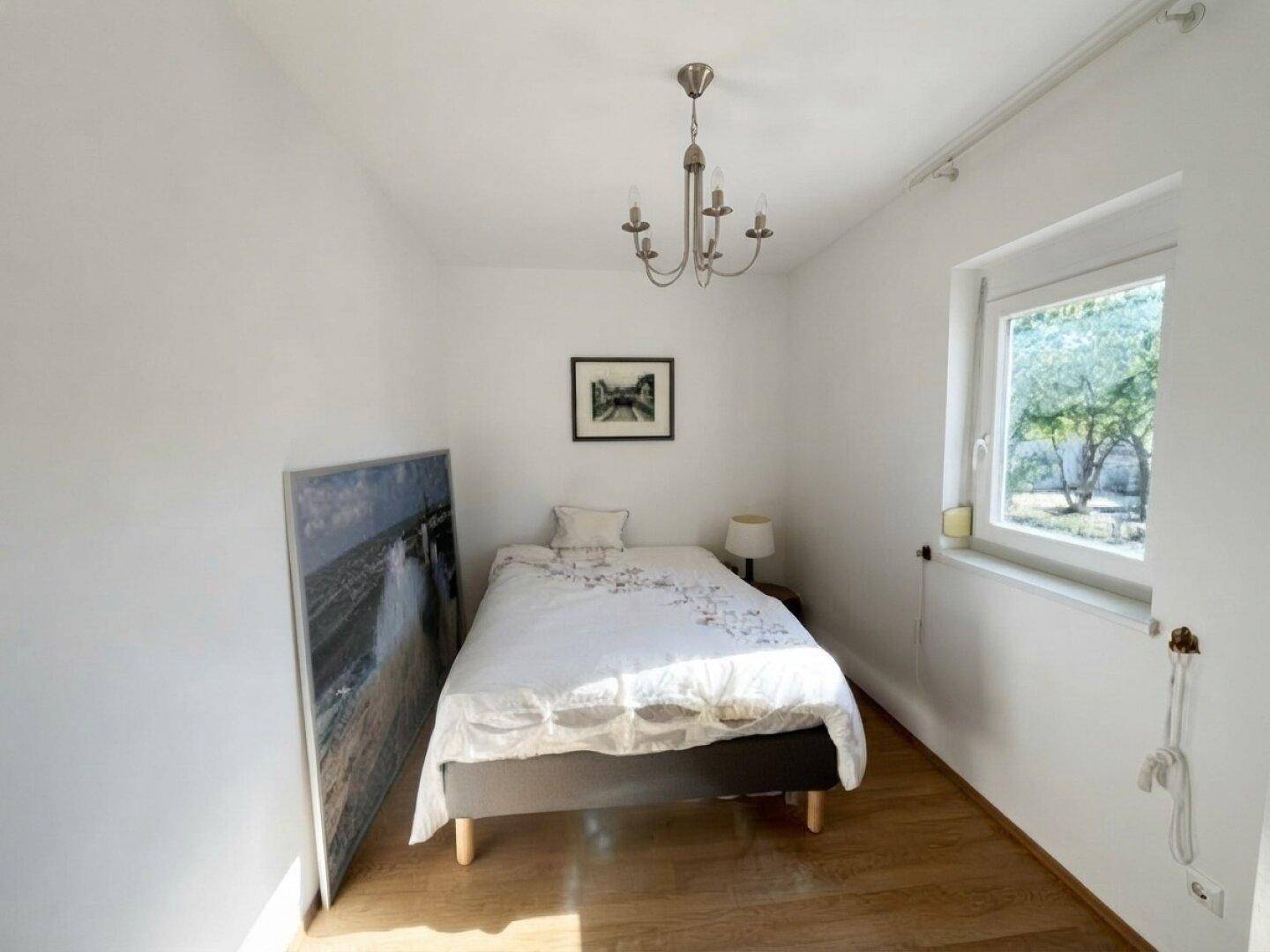 Helles Schlafzimmer mit Holzboden, Fenster und schlichter Einrichtung, ideal zum Entspannen.
