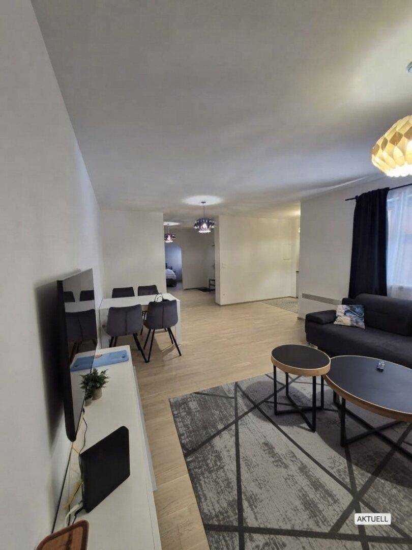 Heller Wohnbereich mit modernem Sofa, Teppich und Esstisch, der eine einladende Atmosphäre schafft.