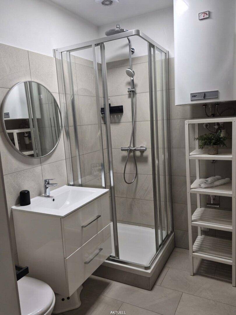Modernes Badezimmer mit Duschkabine, Waschbeckenunterschrank und hellen Fliesen an Wänden und Boden.