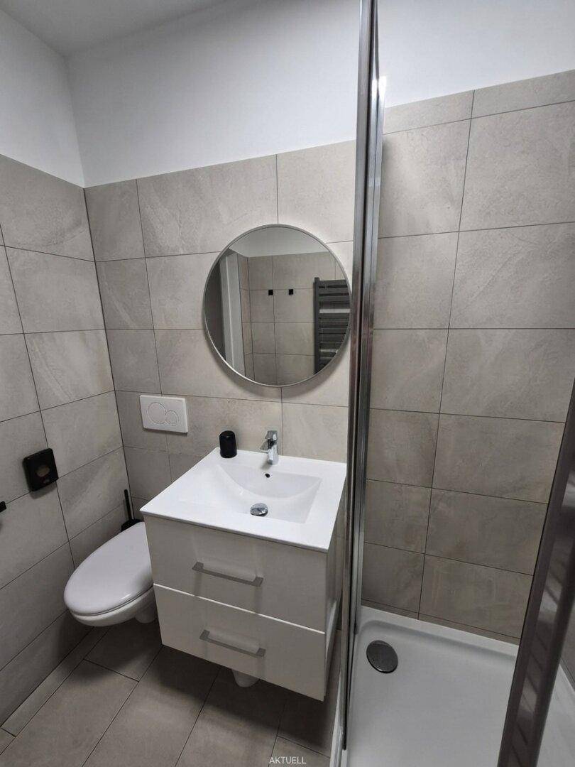 Helles Badezimmer mit wandhängendem WC, modernem Waschbecken und großformatigen Fliesen.