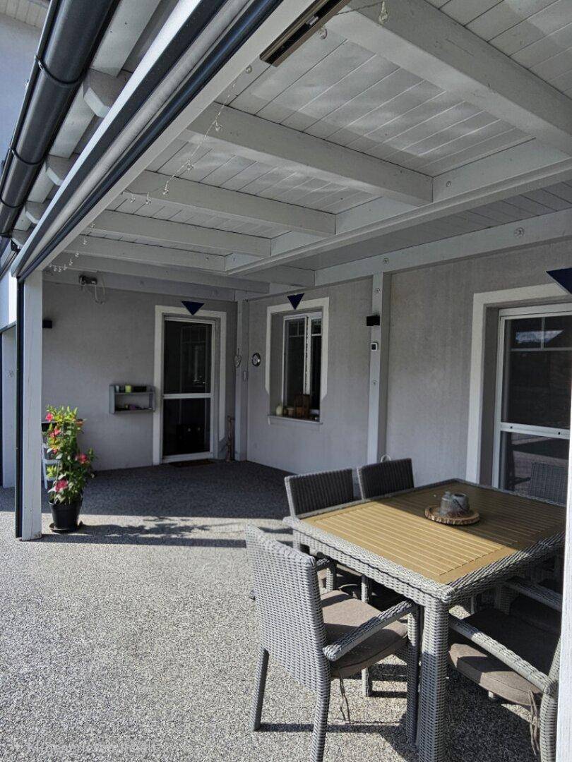 Überdachte Terrasse mit Esstisch und Stühlen, ideal für Mahlzeiten im Freien.
