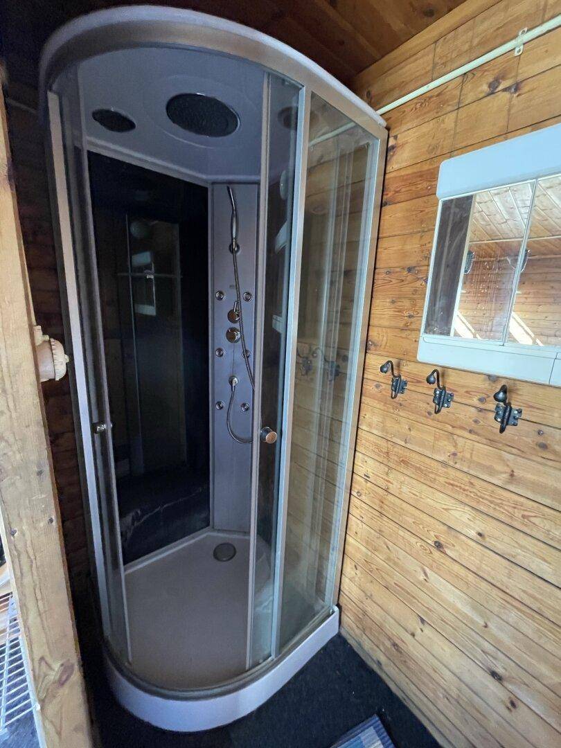 Kleine Duschkabine in einem Badezimmer mit rustikaler Holzvertäfelung.