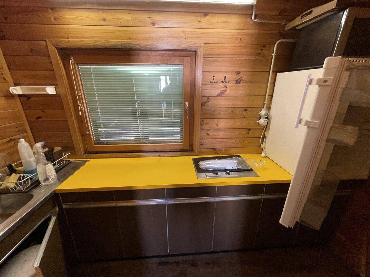 Kleine Küche mit gelber Arbeitsplatte, integriertem Kochfeld und Kühlschrank.