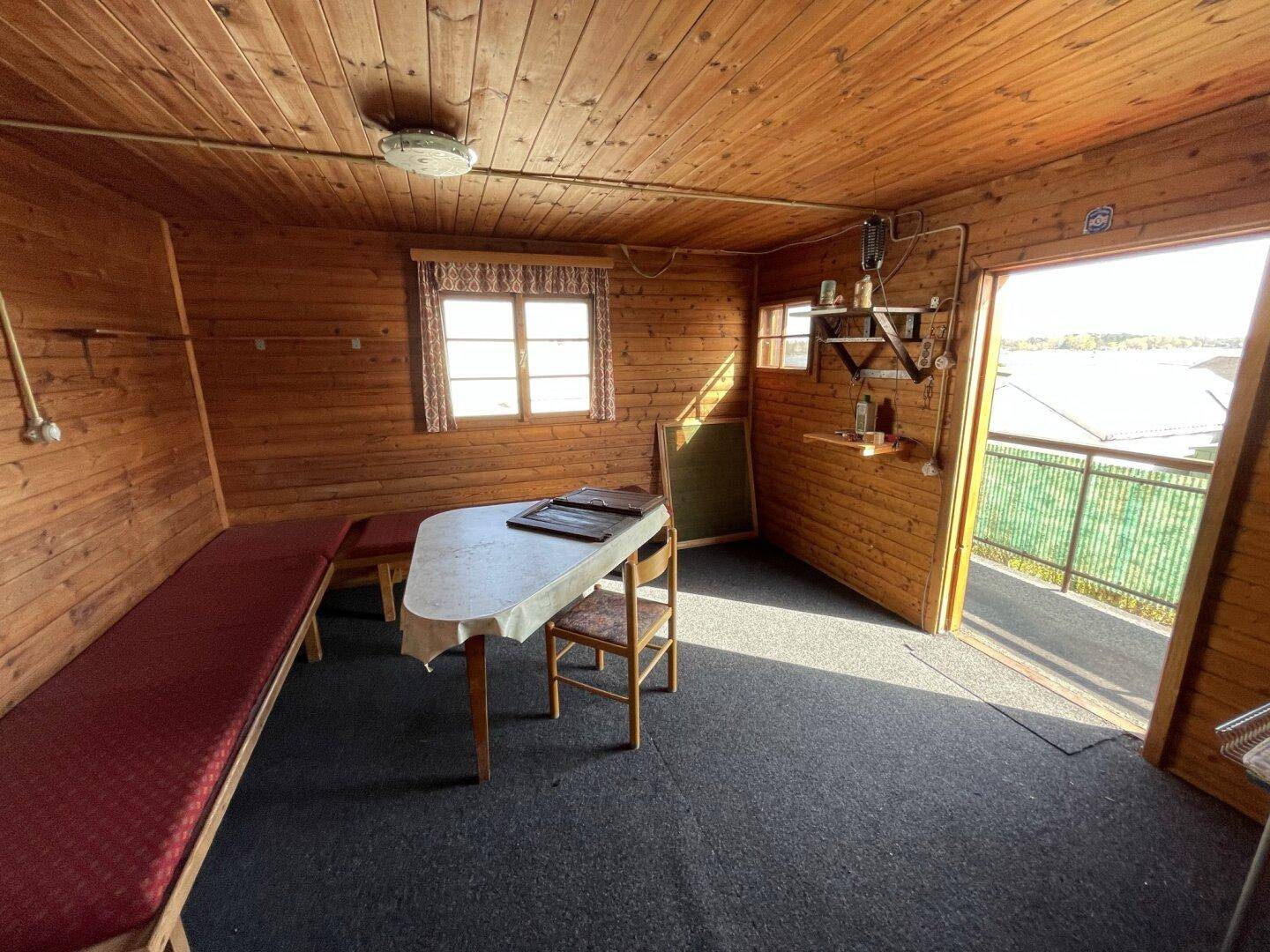 Heller Wohnraum mit Holzvertäfelung, Sitzbänken und Zugang zum Balkon mit Seeblick.