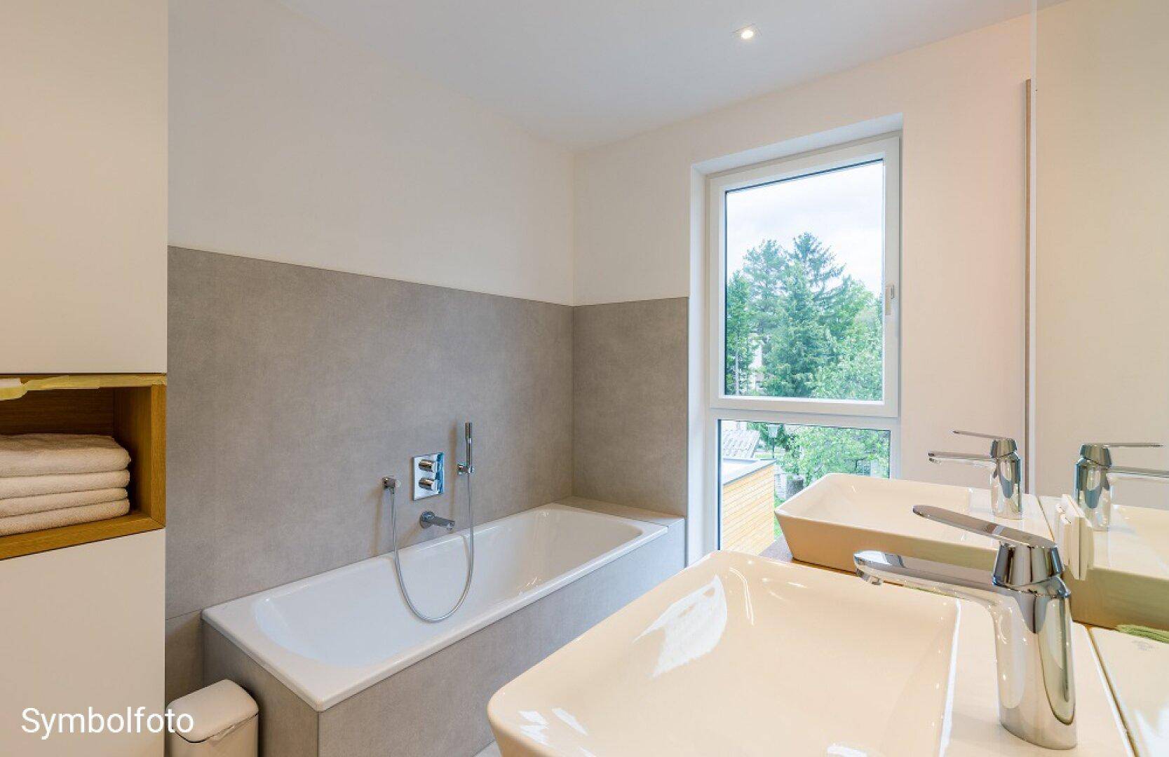 Modernes Badezimmer mit Badewanne, Doppelwaschbecken und Fenster mit Blick ins Grüne.
