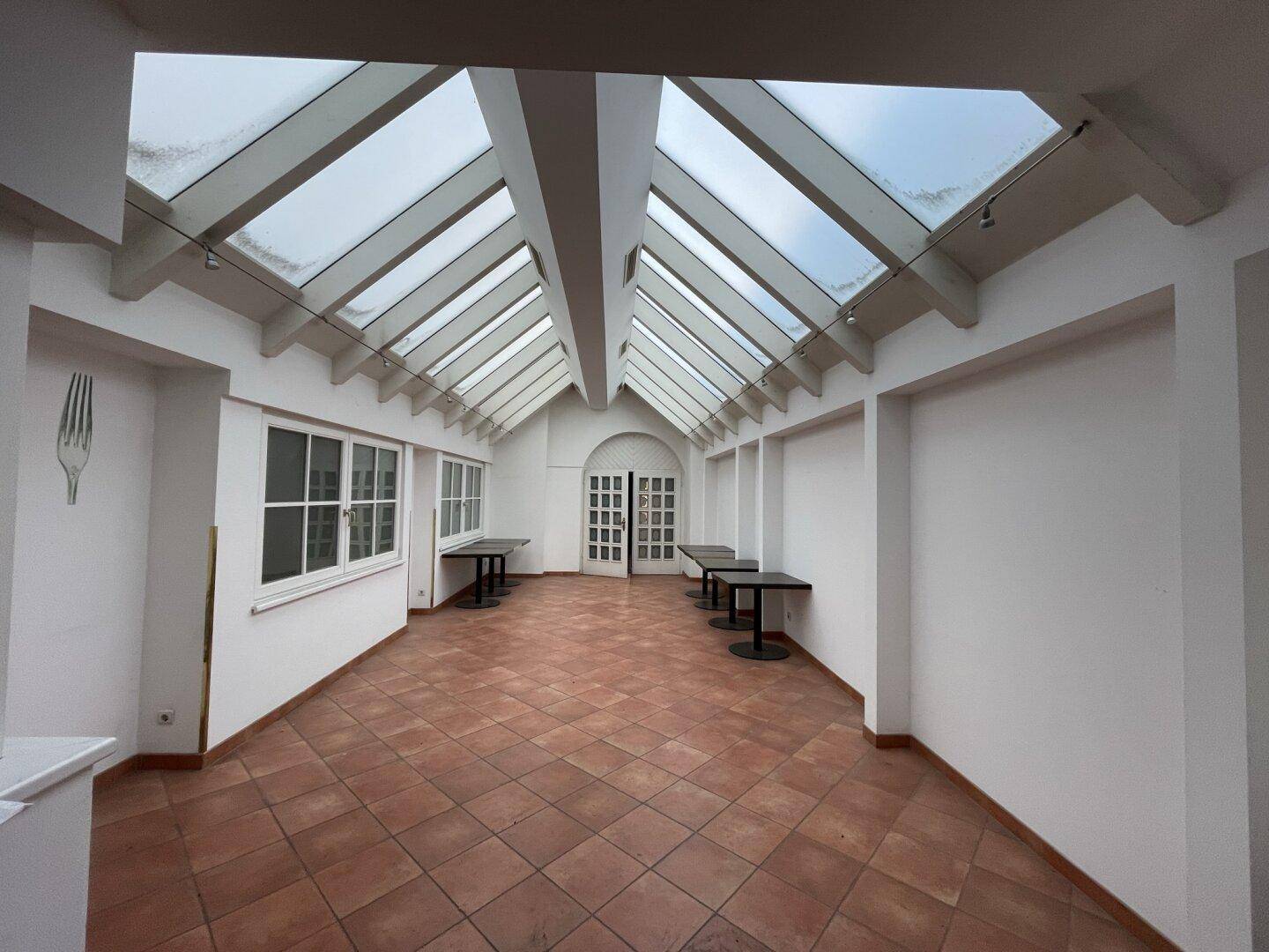 Heller, großer Raum mit Glasdach und Terrakottafliesen, ideal für Veranstaltungen oder als Wintergarten.