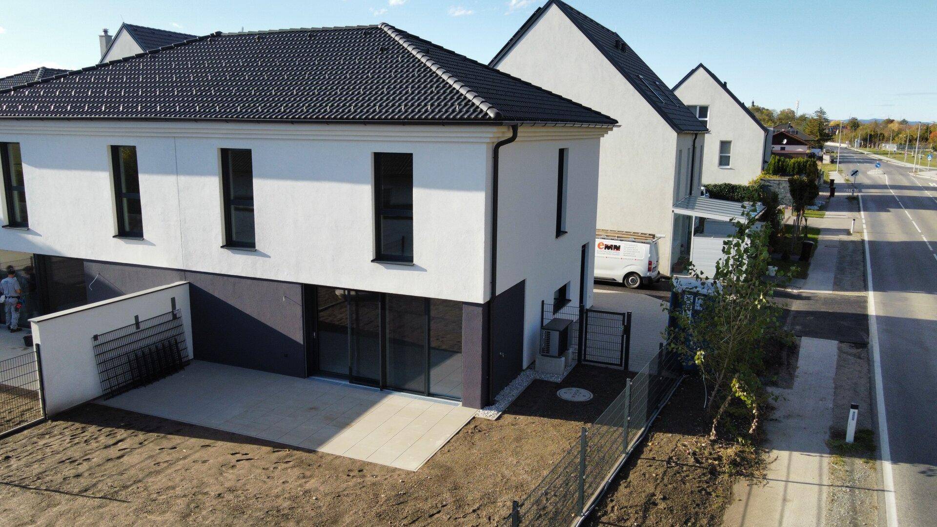 Neubau-Doppelhaushälfte mit weißer Fassade, dunklem Dach und angrenzender Straße im Wohngebiet.
