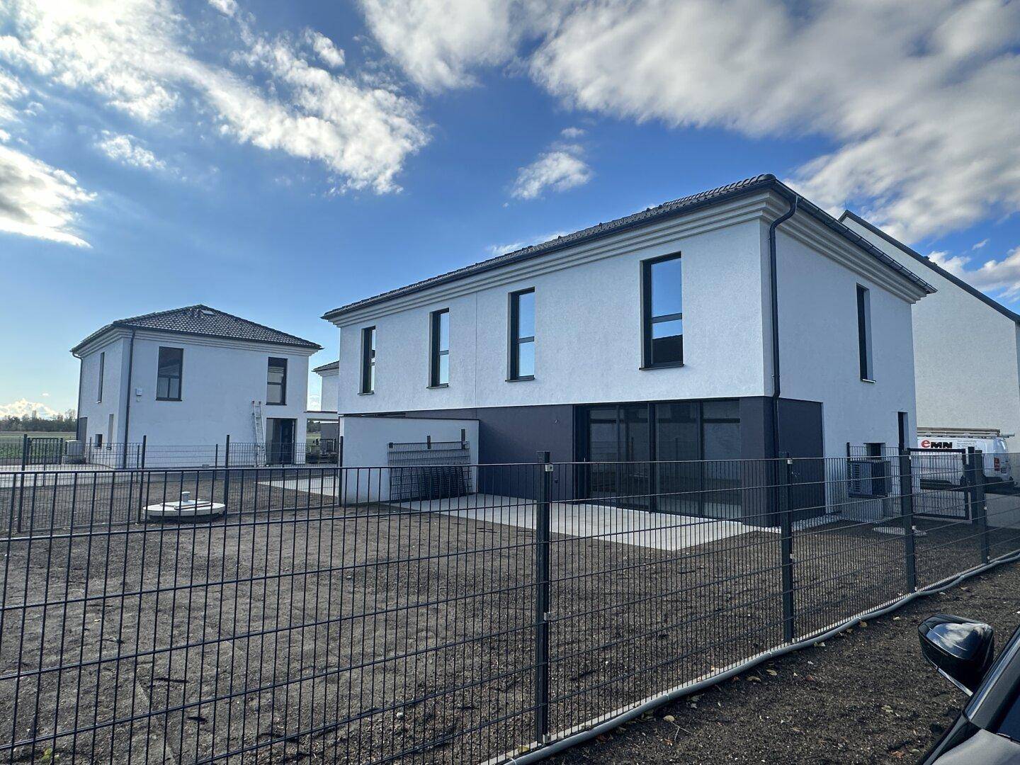Moderne Doppelhaushälfte im Rohbauzustand mit weißer Fassade und unfertigem Außenbereich.