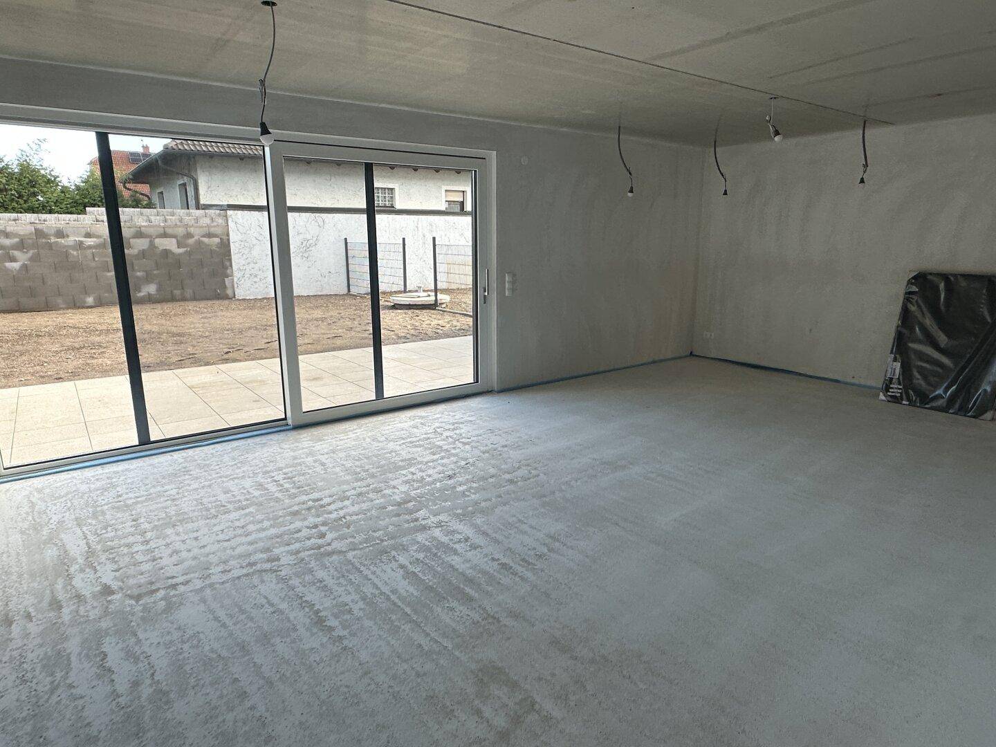 Unfertiger Wohnbereich im Rohbau mit großen Schiebetüren zum Garten und Betonboden.