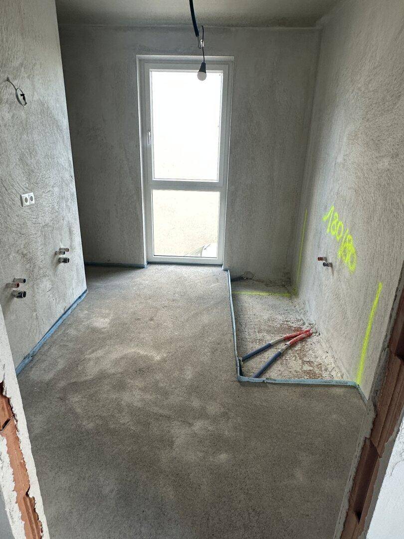Rohbau-Badezimmer mit vorbereiteten Anschlüssen für Sanitäranlagen und einem Fenster.