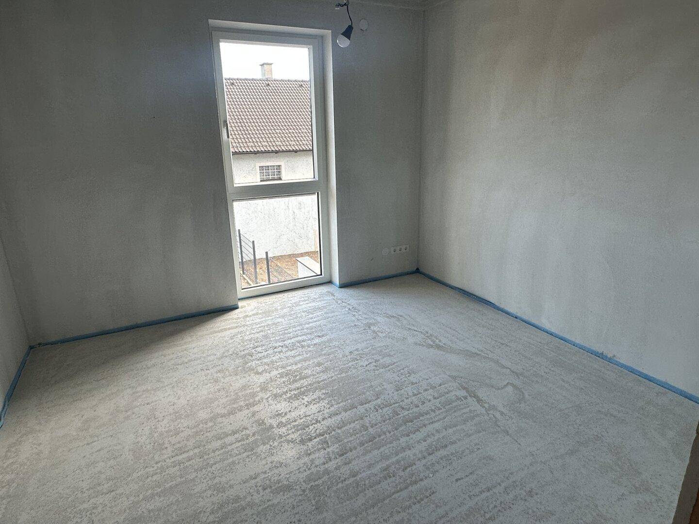 Unfertiges Schlafzimmer im Rohbau mit Fenster und Betonboden, bereit für den Ausbau.