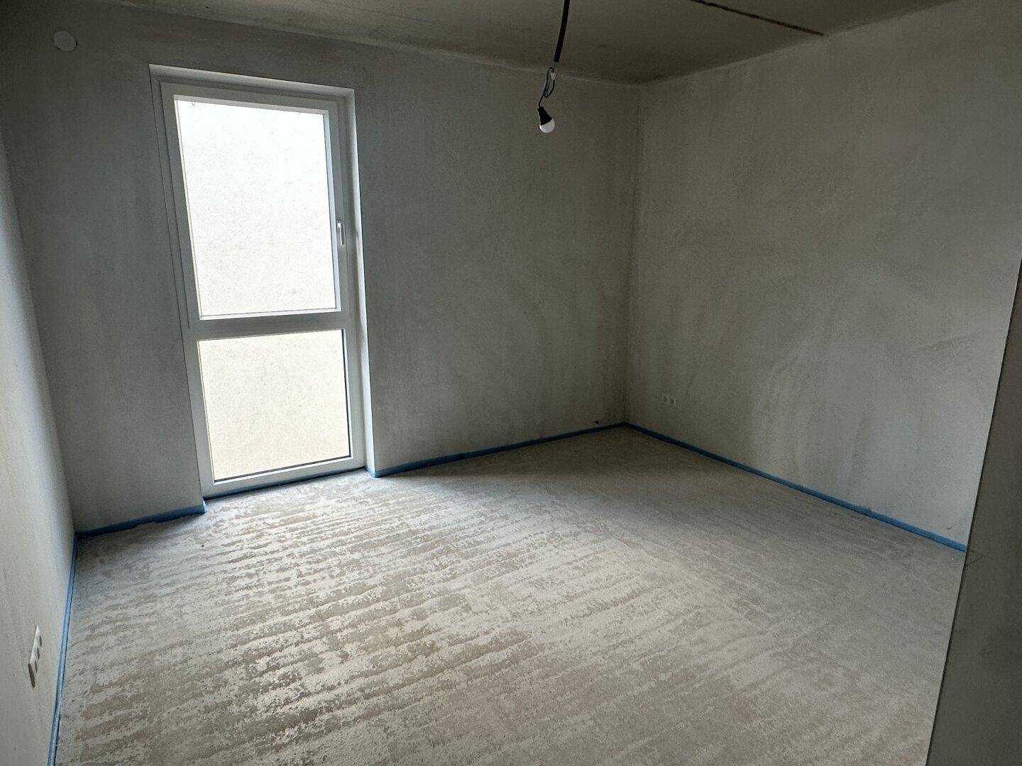 Rohbau-Zimmer mit Fenster und Betonboden, wartet auf die Fertigstellung der Innenarbeiten.